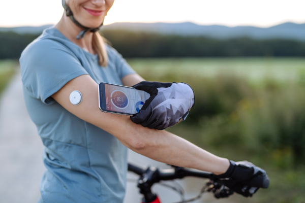 Diabetic cyclist connecting continuous glucose monitor with her smartphone to monitor her blood sugar levels in real time. Concept of exercise and diabetes.