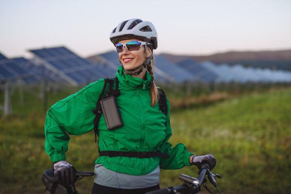 Portrait of a beautiful cyclist standing in front of solar panels at a solar farm during a summer bike tour in nature. A solar farm as solution for more sustainable energy future.