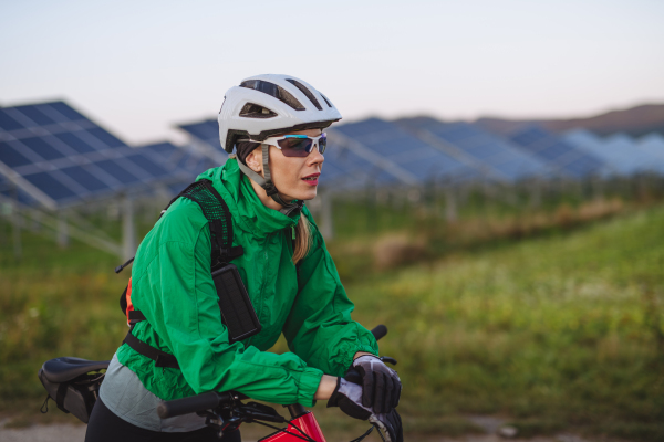 Portrait of a beautiful cyclist standing in front of solar panels at a solar farm during a summer bike tour in nature. A solar farm as solution for more sustainable energy future.