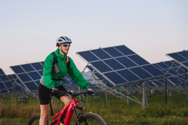 Portrait of a beautiful cyclist riding in front of solar panels at a solar farm during a summer bike tour in nature. A solar farm as solution for more sustainable energy future.