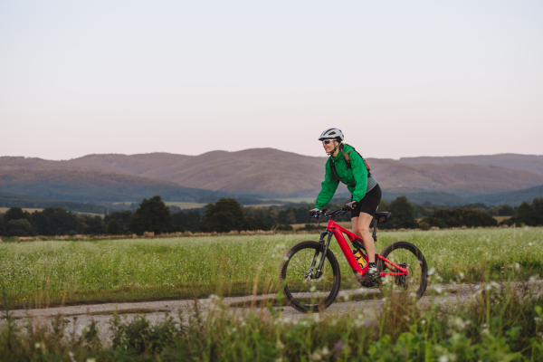 Side view of a female cyclist on an electric bike, riding on a dusty trail in nature. The woman on her bike tour enjoying the beautiful scenery and landscape views.