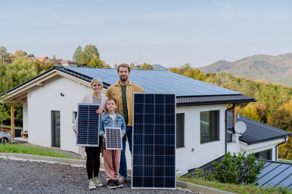 A happy family near their house with solar panels. Alternative energy, saving resources and sustainable lifestyle concept.