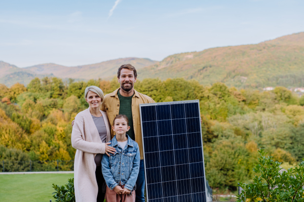 A happy family near their house with solar panel. Alternative energy, saving resources and sustainable lifestyle concept.