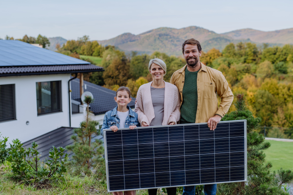 A happy family near their house with solar panel. Alternative energy, saving resources and sustainable lifestyle concept.