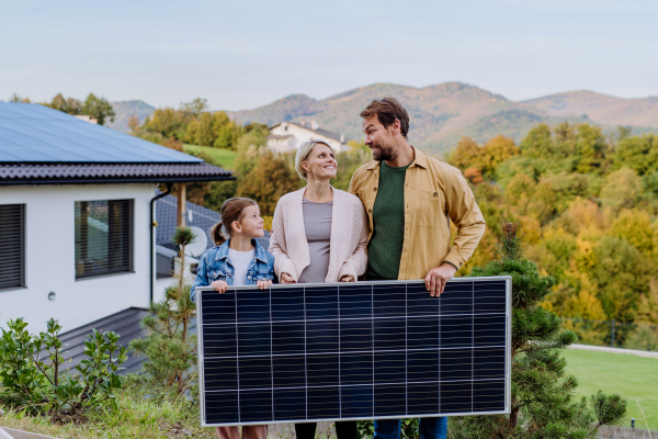 A happy family near their house with solar panel. Alternative energy, saving resources and sustainable lifestyle concept.