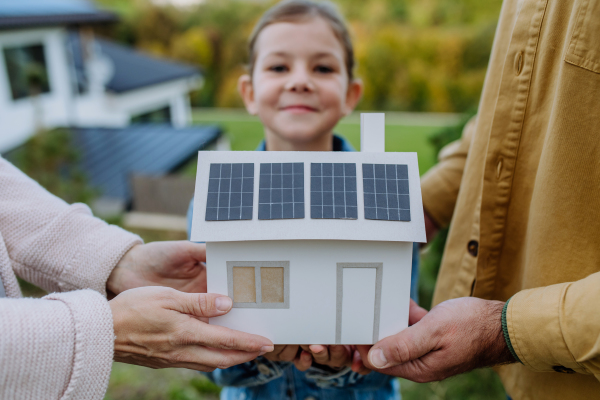 Close up of young family holding paper model of house with the solar panels.Alternative energy, saving resources and sustainable lifestyle concept.