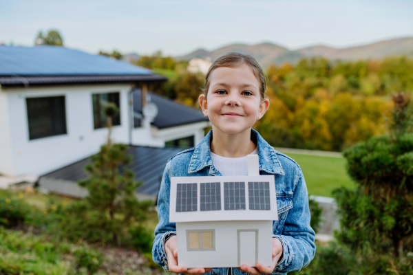 Close up of happy girl holding paper model of house with the solar panels.Alternative energy, saving resources and sustainable lifestyle concept.