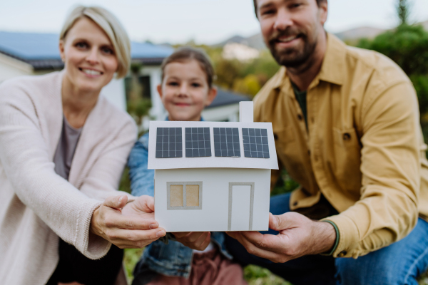 Happy family holding paper model of house with the solar panels.Alternative energy, saving resources and sustainable lifestyle concept.