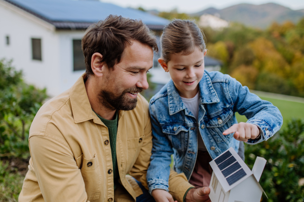 Little girl with her father holding paper model of house with the solar panels, explaining how it works.Alternative energy, saving resources and sustainable lifestyle concept.