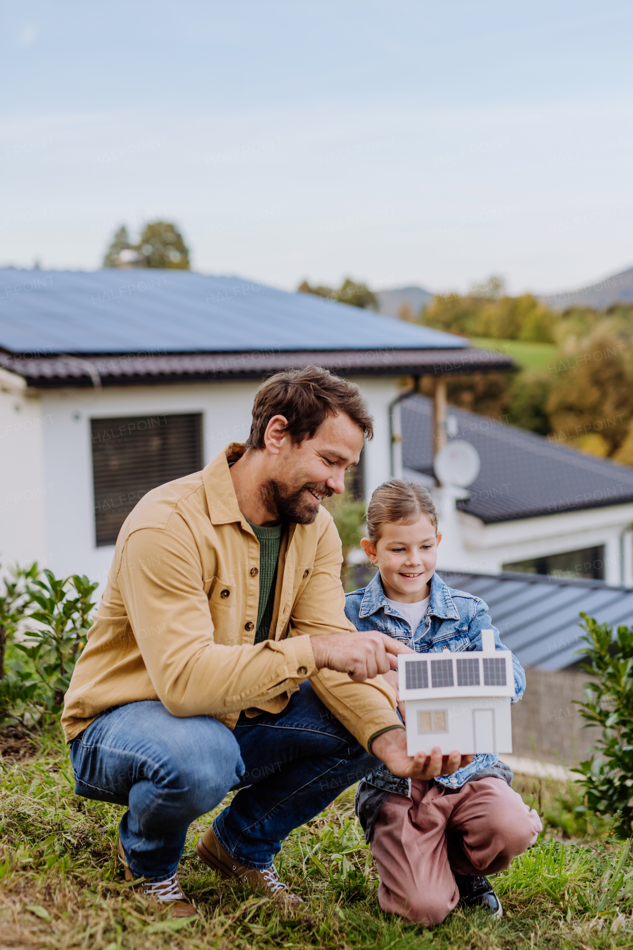 Little girl with her father holding paper model of house with the solar panels, explaining how it works.Alternative energy, saving resources and sustainable lifestyle concept.