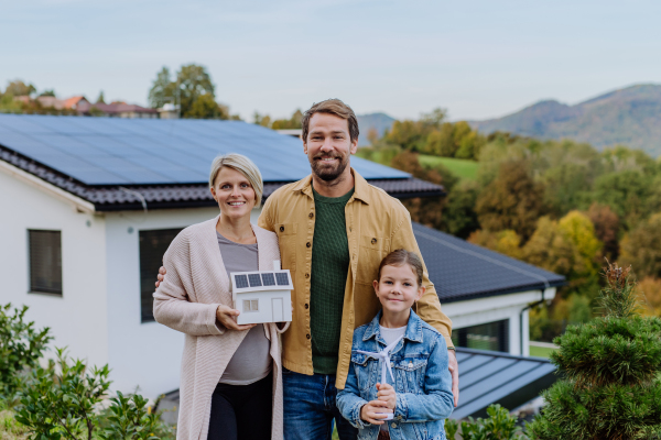 Happy family holding paper model of house with the solar panels.Alternative energy, saving resources and sustainable lifestyle concept.