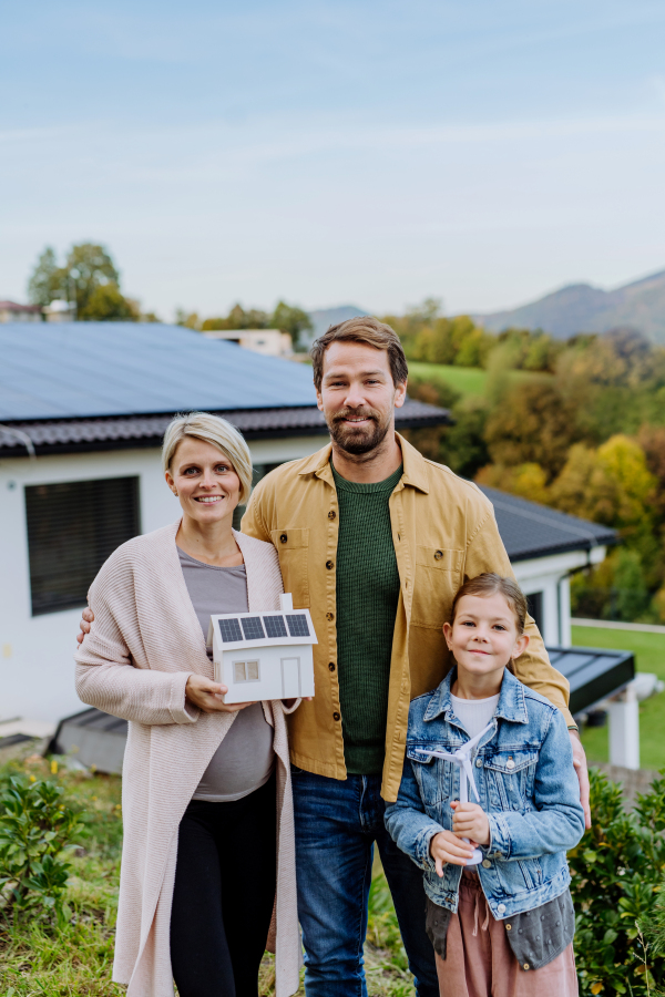 Happy family holding paper model of house with the solar panels.Alternative energy, saving resources and sustainable lifestyle concept.