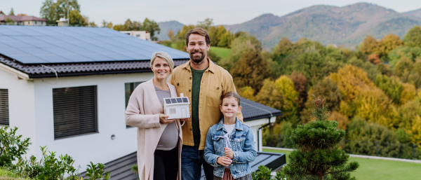 Happy family holding paper model of house with the solar panels.Alternative energy, saving resources and sustainable lifestyle concept.