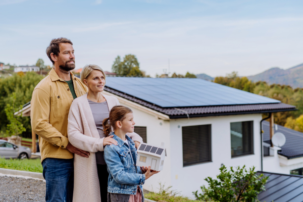 Happy family holding paper model of house with the solar panels.Alternative energy, saving resources and sustainable lifestyle concept.