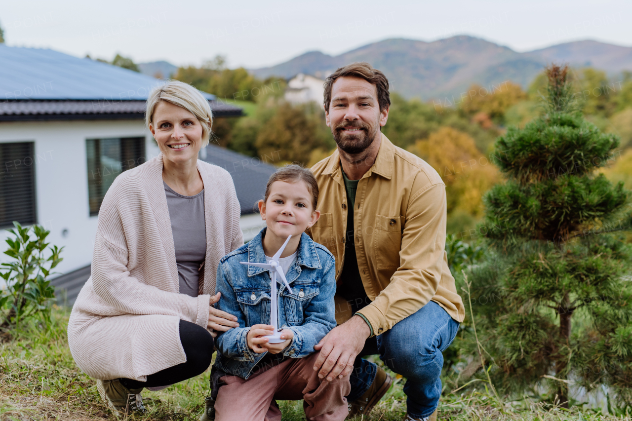 Happy family holding a plastic model of wind turbine. Alternative energy, saving resources and sustainable lifestyle concept.