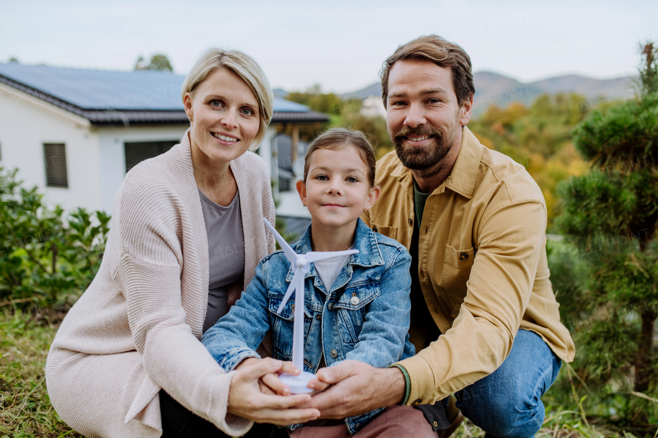 Happy family holding a plastic model of wind turbine. Alternative energy, saving resources and sustainable lifestyle concept.