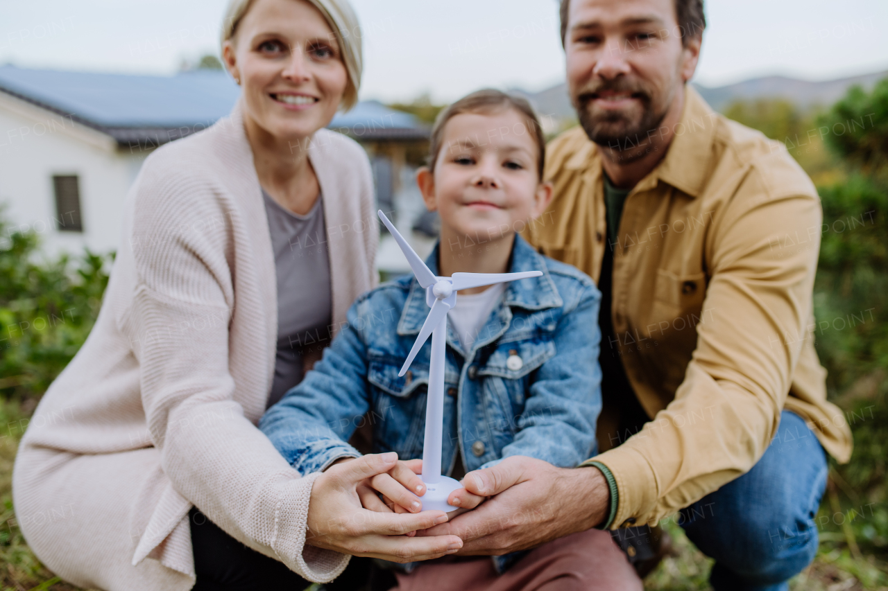 Happy family holding a plastic model of wind turbine. Alternative energy, saving resources and sustainable lifestyle concept.