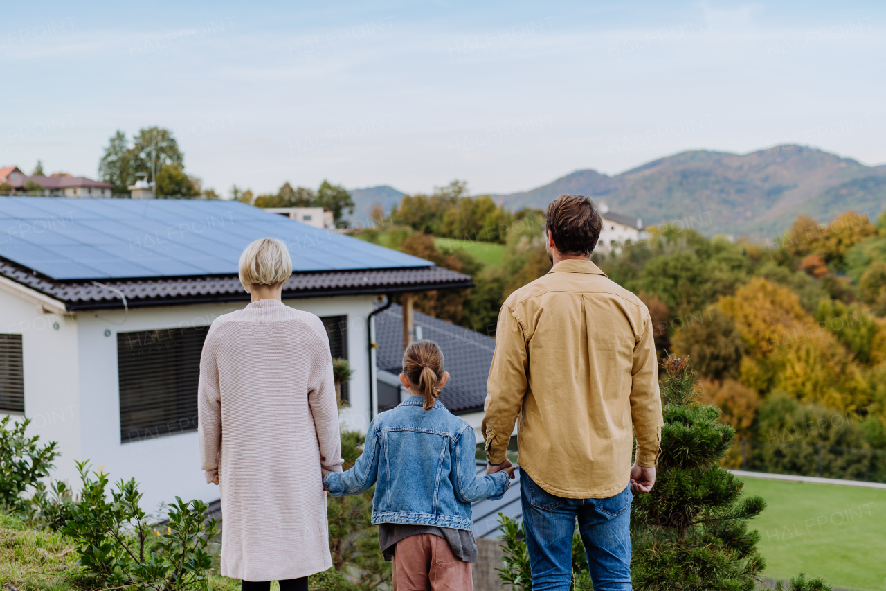 Rear view of family looking at their house with solar panels.Alternative energy, saving resources and sustainable lifestyle concept.