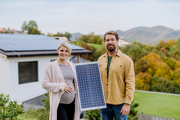 A happy couple near their house with solar panels. Alternative energy, saving resources and sustainable lifestyle concept.