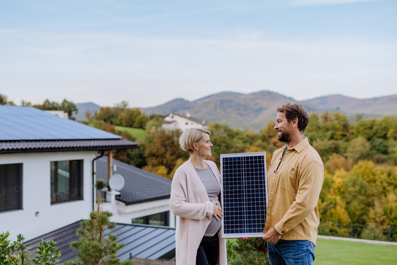 A happy couple near their house with solar panels. Alternative energy, saving resources and sustainable lifestyle concept.