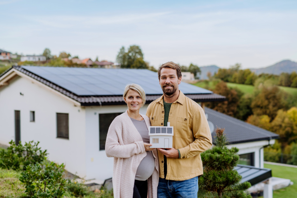 Close-up of happy couple holding paper model of house with solar panels. Alternative energy, saving resources and sustainable lifestyle concept.