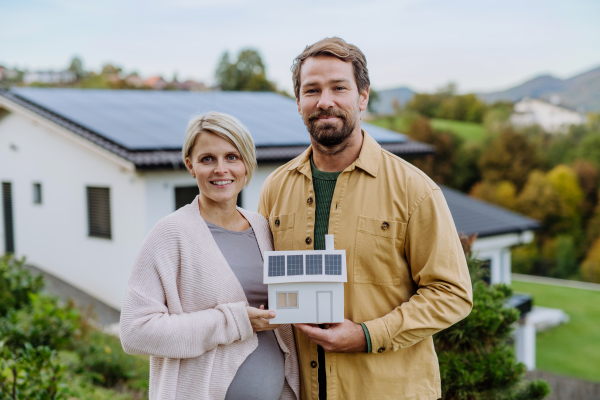 Close-up of happy couple holding paper model of house with solar panels. Alternative energy, saving resources and sustainable lifestyle concept.