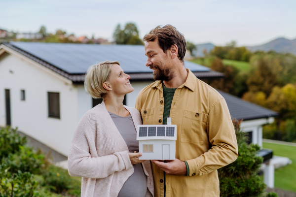 Close-up of happy couple holding paper model of house with solar panels. Alternative energy, saving resources and sustainable lifestyle concept.