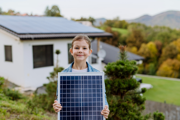 Little girl holding a photovoltaics solar panel. Alternative energy, saving resources and sustainable lifestyle concept.