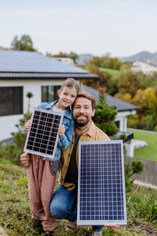 Father with his little daughter near the house with solar panels. Alternative energy, saving resources and sustainable lifestyle concept.