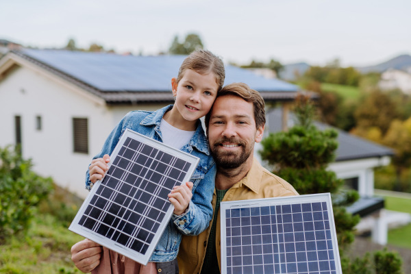 Father with his little daughter near the house with solar panels. Alternative energy, saving resources and sustainable lifestyle concept.