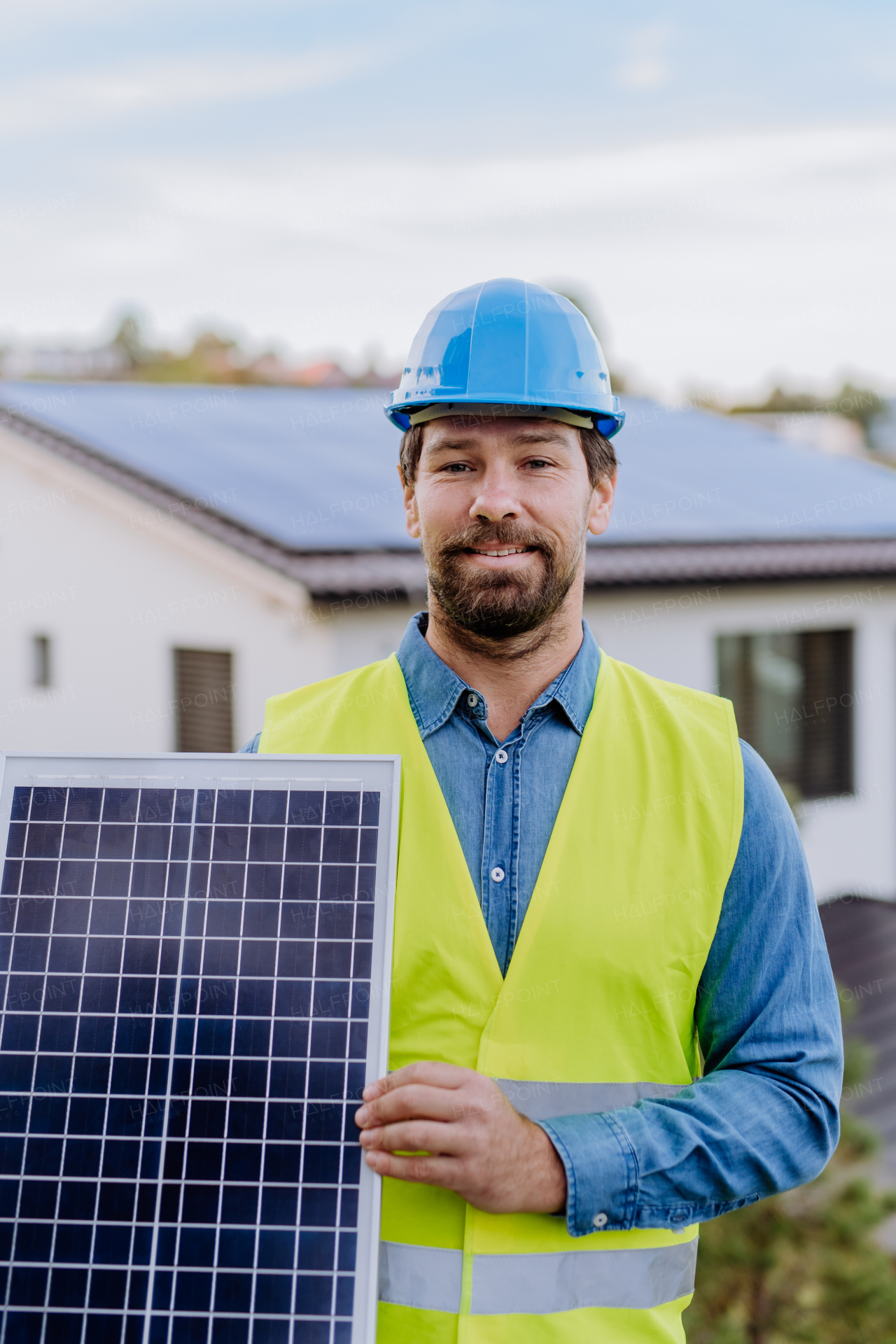 A smiling handyman solar installer carrying solar module while installing solar panel system on house.