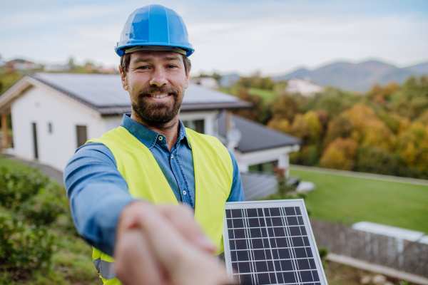 Smiling handyman, photovoltaics panels installer shaking hand with owner of the house.