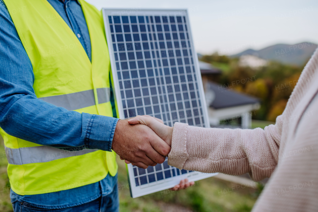 Close-up od handyman, photovoltaics panels installer shaking hand with owner of the house.