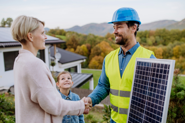 Smiling handyman, photovoltaics panels installer shaking hand with family owner of the house.