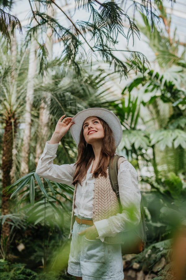 Portrait of a young woman with hat and backpack in botanical garden. Botanist in greenhouse.