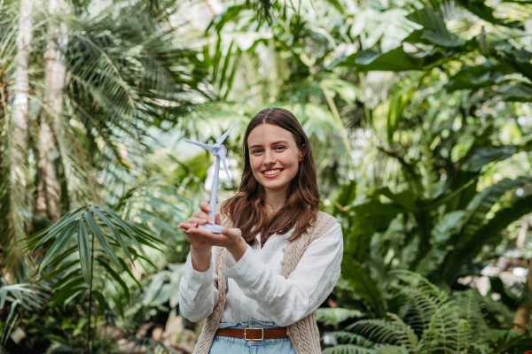 Young woman in greenhouse holding model of wild turbine, concept of renewable energy and protection of nature.