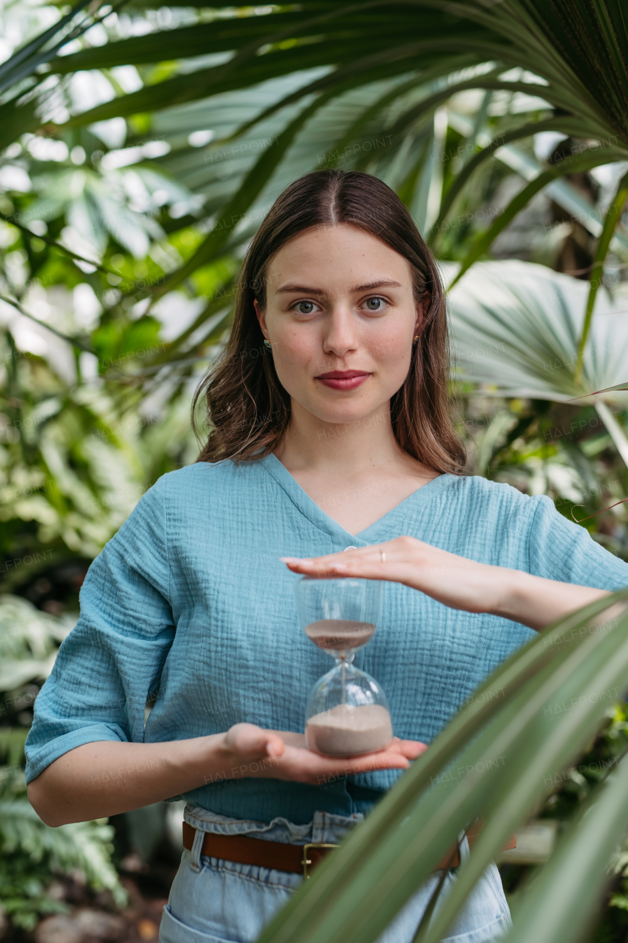 Young woman with a hourglass in jungle, concept of nature protection.