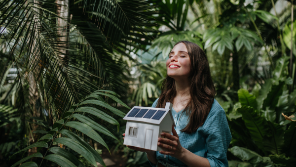 Young woman in jungle holding model of house with solar panels, concept of renewable energy and protection of nature.