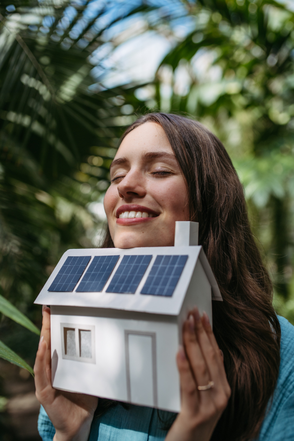 Young woman in jungle holding model of house with solar panels, concept of renewable energy and protection of nature.