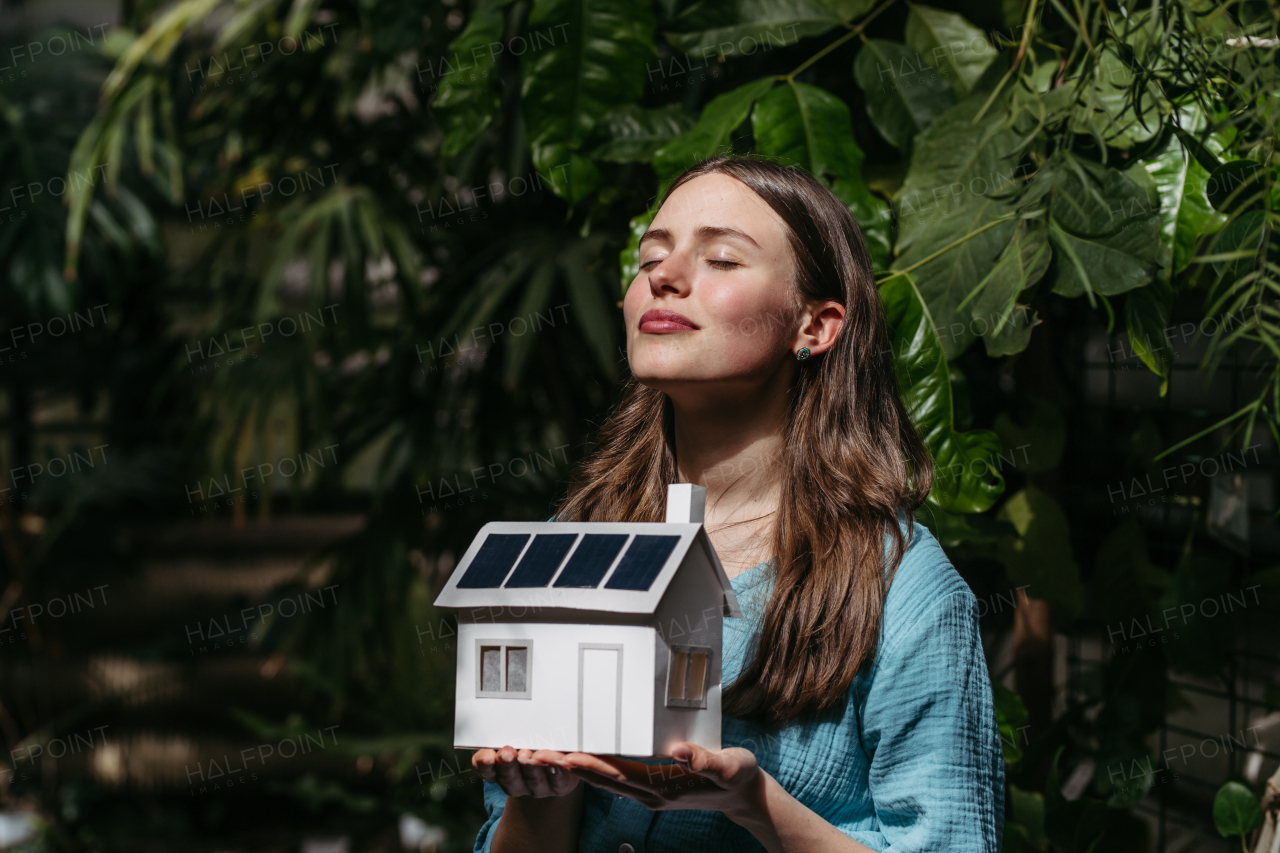 Young woman in jungle holding model of house with solar panels, concept of renewable energy and protection of nature.