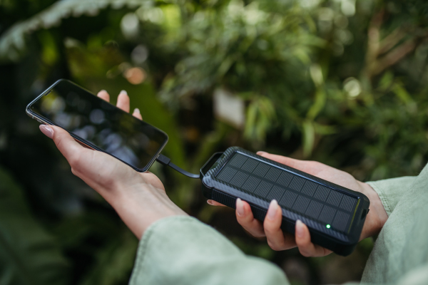 Close up of woman charging her smartphone with solar power bank, outdoor in nature.