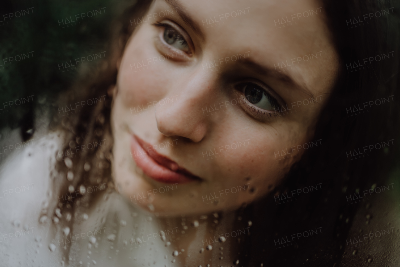 Portrait of a young woman in misty greenhouse through foggy glass with water droplets.