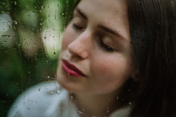 Portrait of a young woman in misty greenhouse through foggy glass with water droplets.