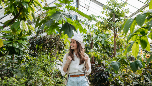 Portrait of a young woman with hat and backpack in botanical garden. Botanist in greenhouse.