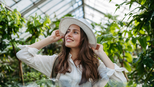 Portrait of a young woman with hat and backpack in botanical garden. Botanist in greenhouse.