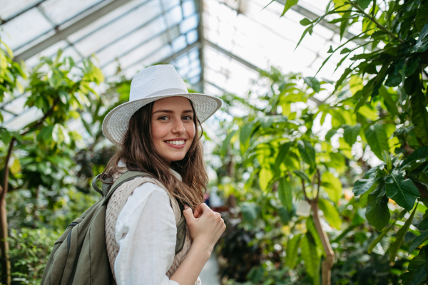 Portrait of a young woman with hat and backpack in botanical garden. Botanist in greenhouse.