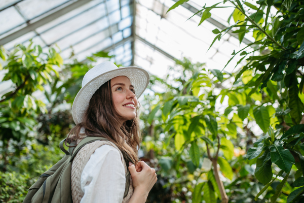 Portrait of a young woman with hat and backpack in botanical garden. Botanist in greenhouse.