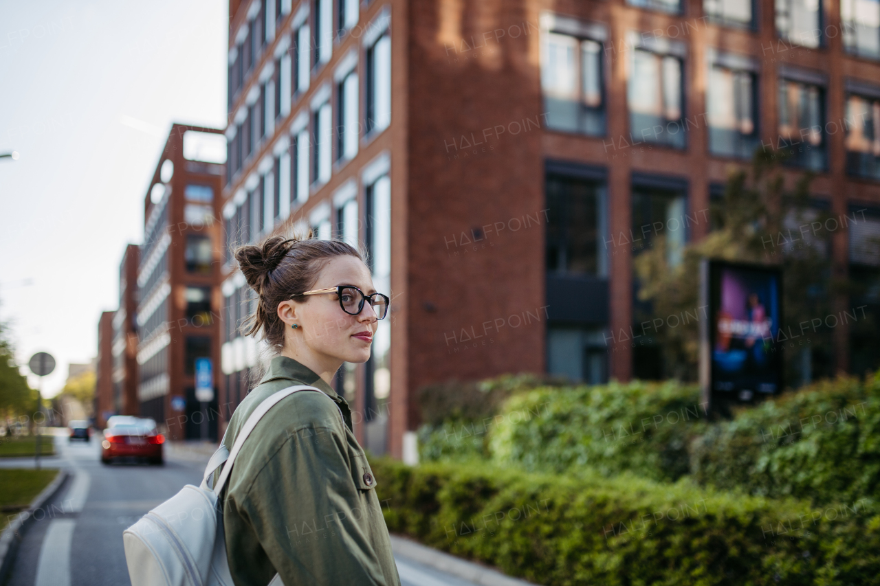 Portrait of young woman wearing glasses on city street, standing in front red brick building.