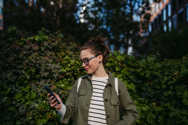 Portrait of young woman scrolling her smartphone and enjoying nature in a city park.