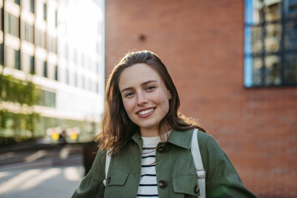 Portrait of a young woman in a city, standing in front red brick building.